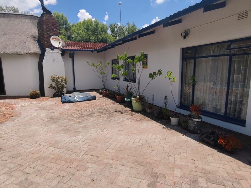 A paved rear courtyard area featuring a brick chimney, thatched roof section, and large windows, providing a functional outdoor space.