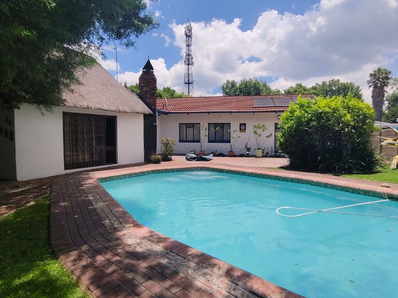 Outdoor pool area featuring a swimming pool with brick paving surround, adjacent to a thatched roof structure and main house exterior.