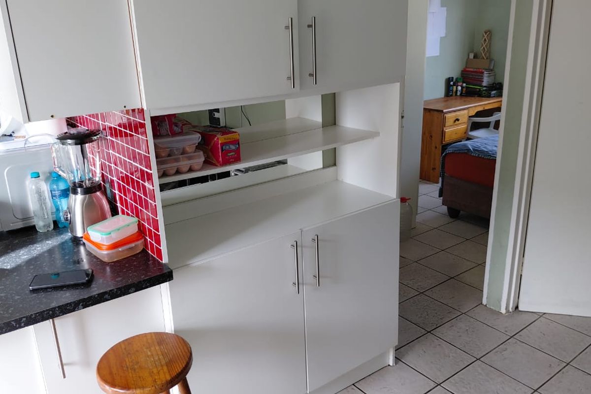 A kitchen area featuring white built-in cabinetry, a vibrant red tiled backsplash, and dark laminate countertops, with tiled flooring throughout.