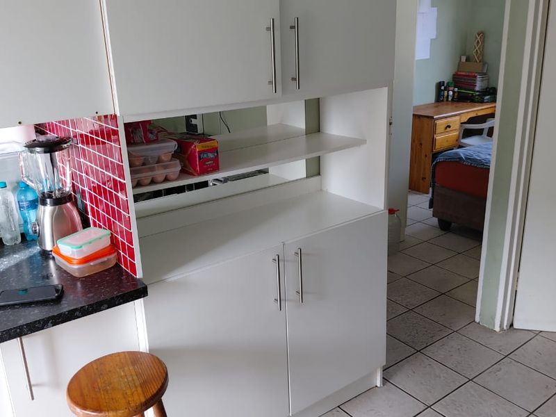 A kitchen area featuring white built-in cabinetry, a vibrant red tiled backsplash, and dark laminate countertops, with tiled flooring throughout.