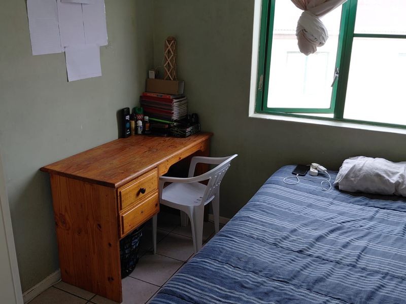 A compact bedroom featuring tiled flooring and a window with an aluminium frame, offering a functional space ready for cosmetic updates.