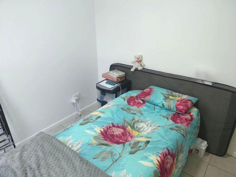 A compact bedroom featuring neutral white walls and tiled flooring, providing a simple and functional living space.