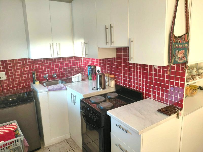 Compact kitchen featuring white cabinetry, a striking red tiled backsplash, laminate countertops, and a freestanding electric stove.