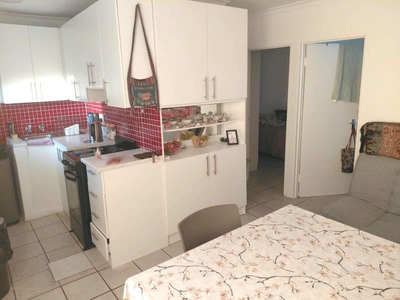 Open plan kitchen and dining area featuring white cabinetry, a red tiled backsplash, and ceramic floor tiles, offering a functional layout for daily living.