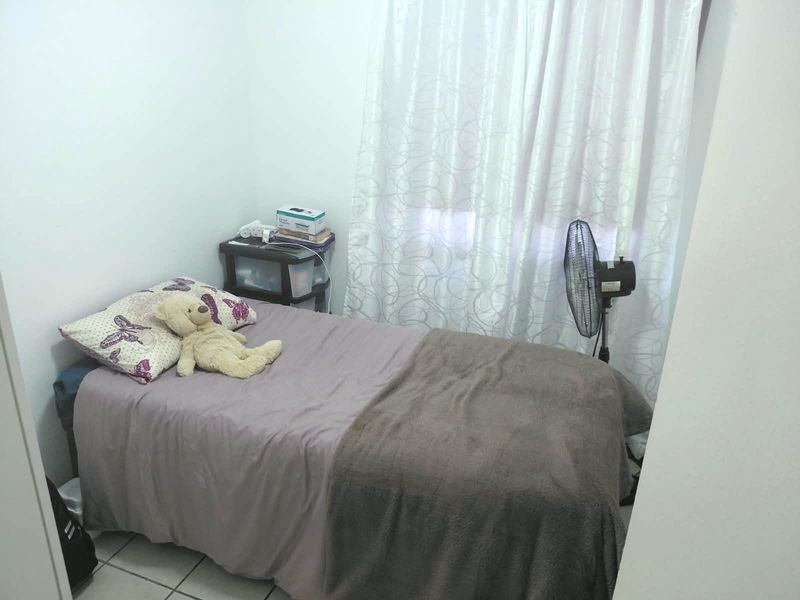 A compact bedroom featuring tiled flooring and window curtains, providing a functional and simple living space.