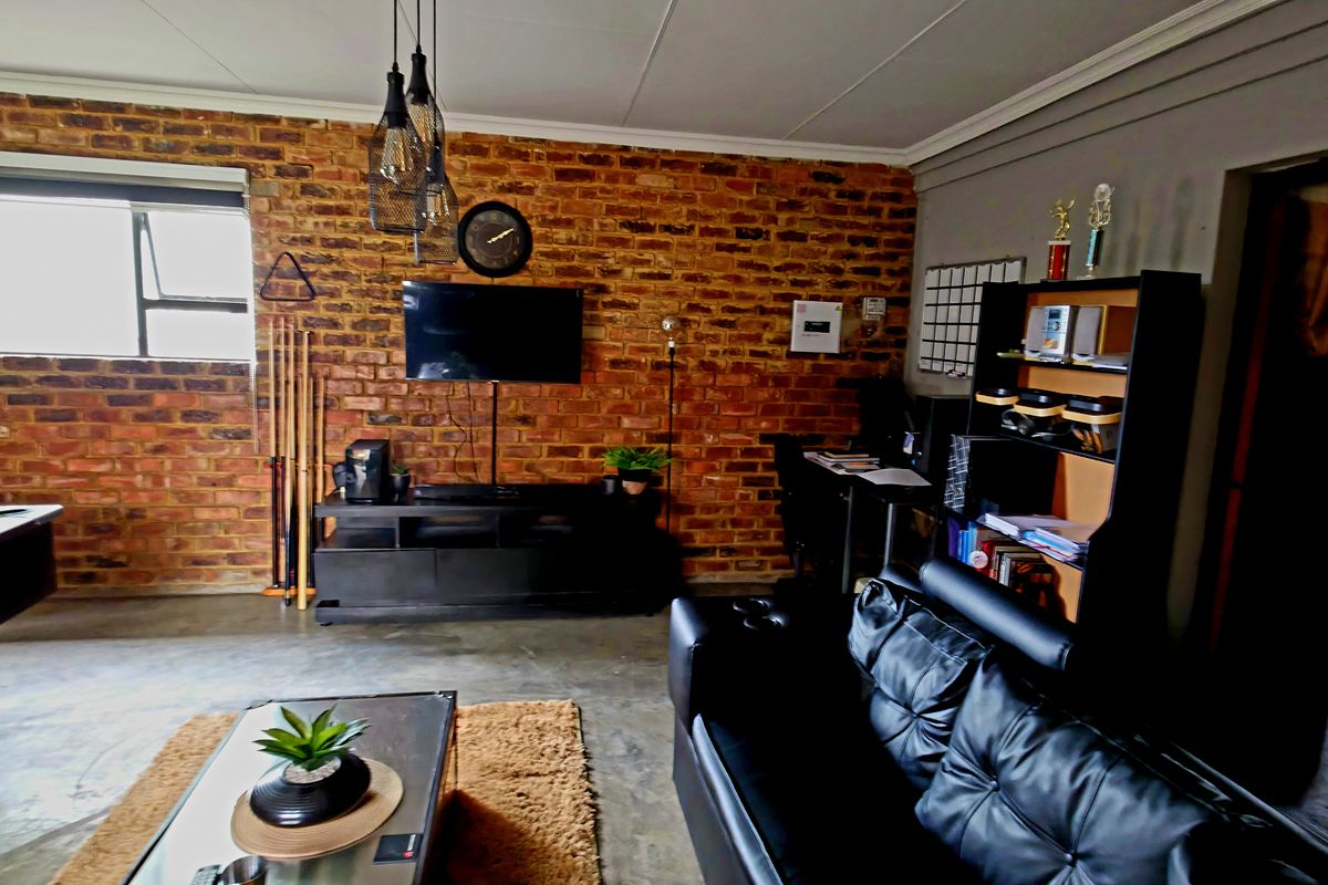 A spacious living area featuring an exposed brick feature wall, polished concrete flooring, and modern pendant lighting, suitable for a lounge or entertainment room.