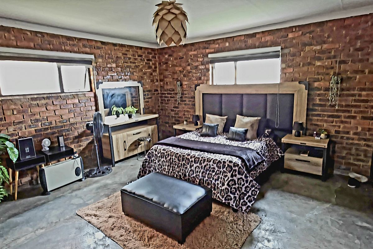 A spacious bedroom featuring exposed face-brick walls, polished concrete flooring, and large windows providing natural light.
