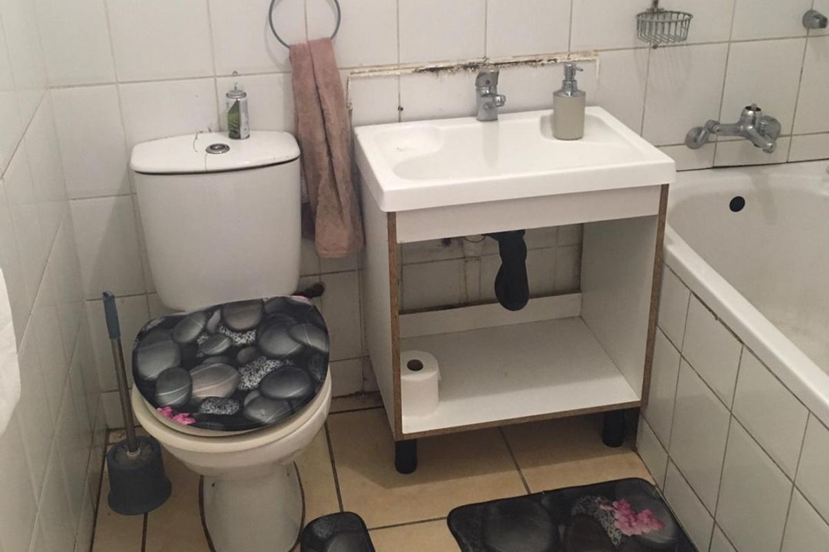 A compact bathroom featuring a standard bathtub, pedestal-style vanity basin, and toilet with white wall and floor tiling.
