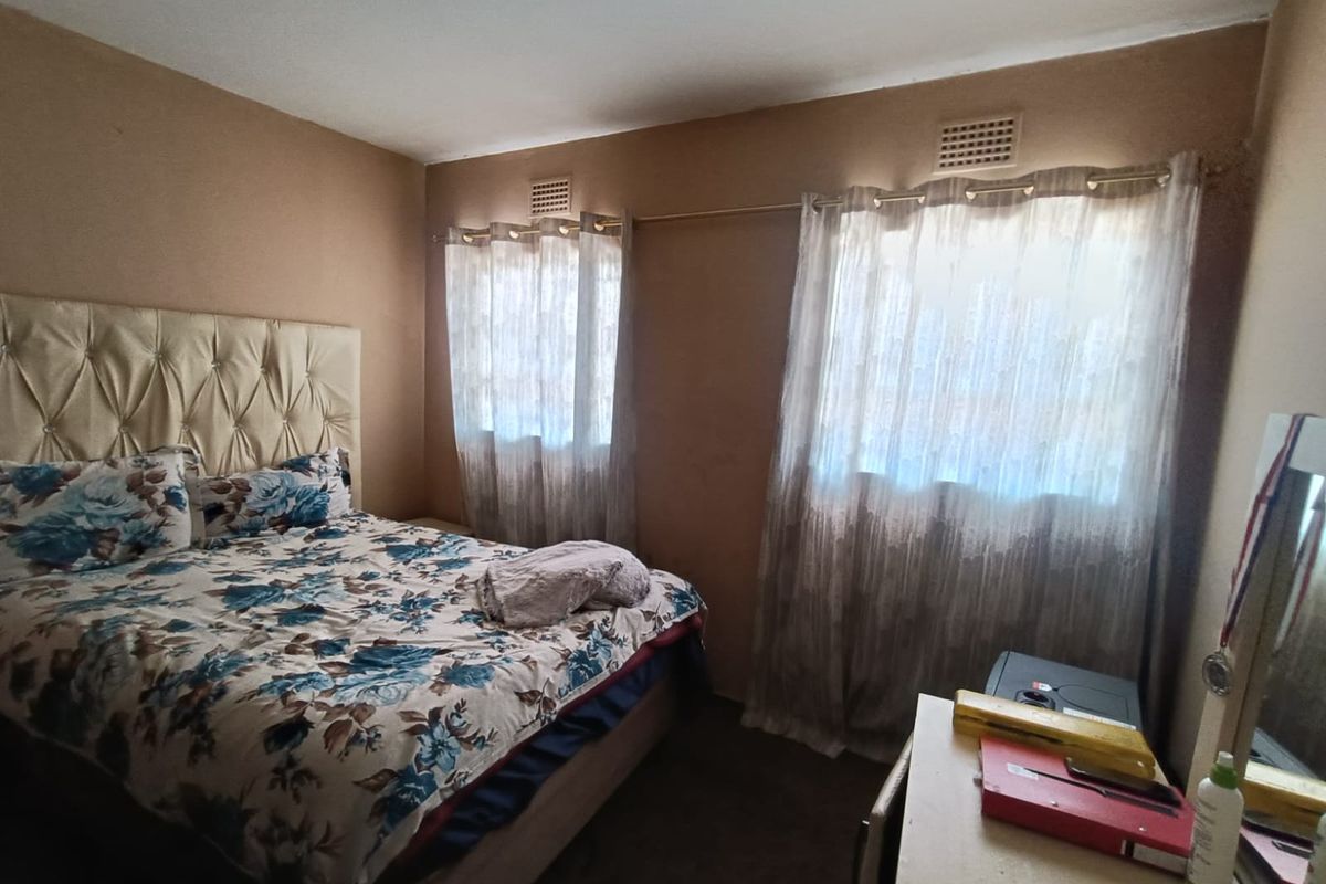 A standard bedroom featuring two windows with ventilation vents and carpeted flooring.