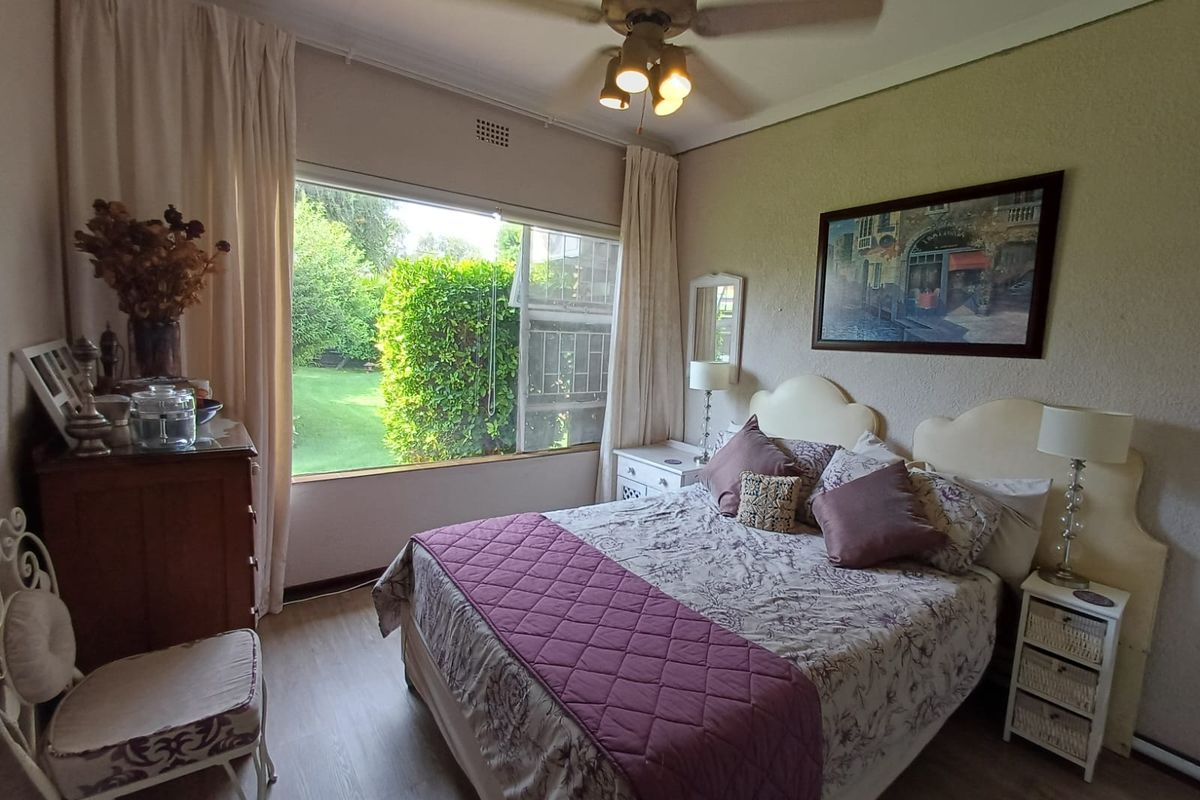 A well-lit bedroom featuring large windows with garden views, neutral wall finishes, and a ceiling fan.