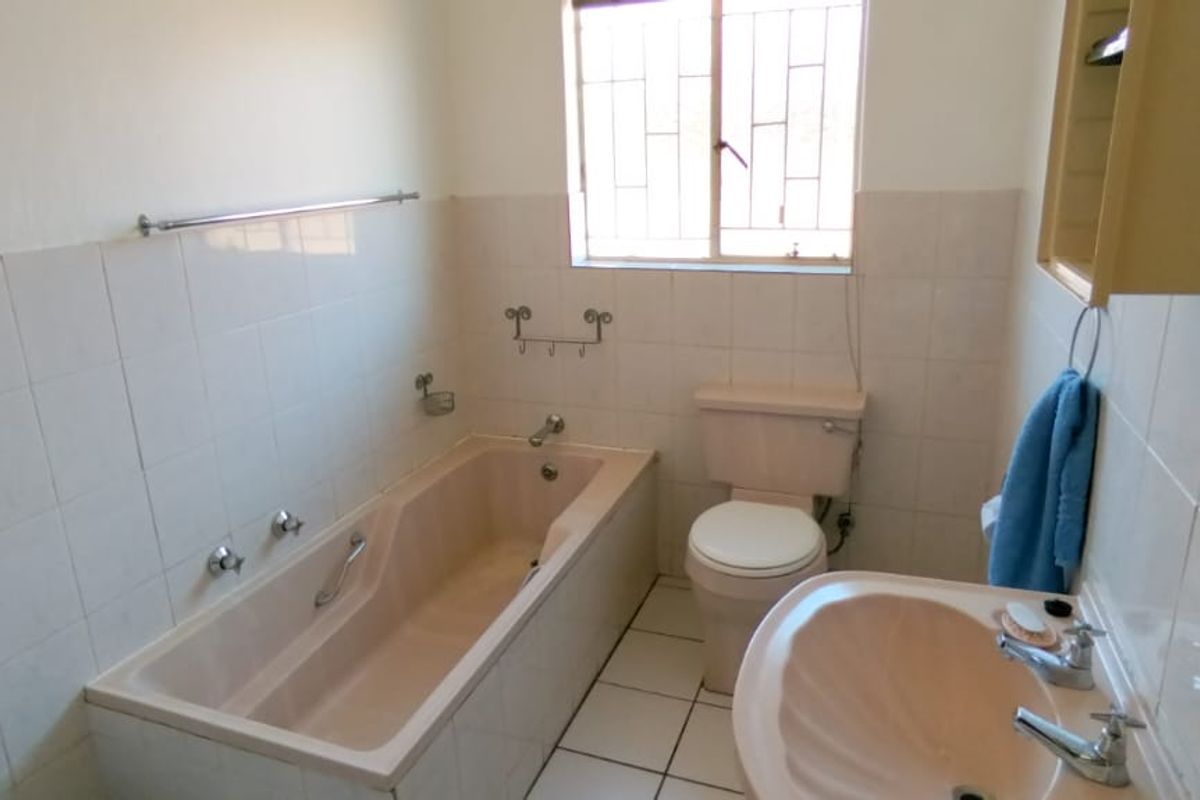 A dated bathroom featuring a pastel-toned bathtub and pedestal basin, tiled walls, and a window with security bars.