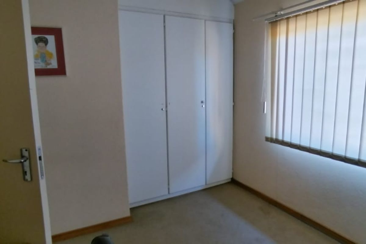 A bedroom featuring built-in cupboards and vertical window blinds, providing a functional space with neutral finishes.