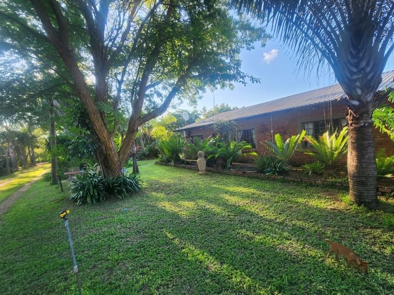 A view of the rear garden and exterior brick facade of the farm property, featuring established trees and landscaped garden beds.