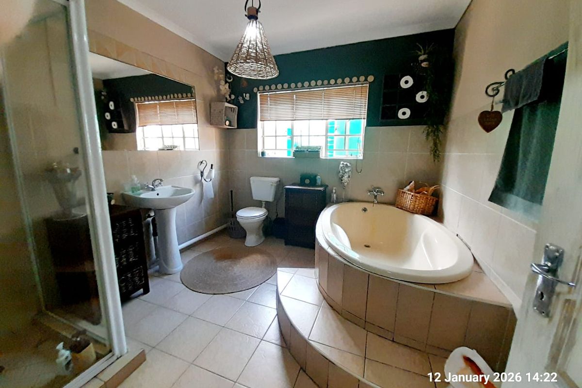 A functional bathroom featuring a raised corner bathtub, separate glass-enclosed shower, pedestal basin, and toilet with tiled flooring and walls.