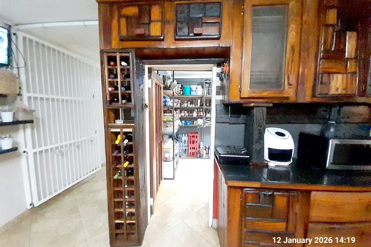A rustic kitchen featuring custom wooden cabinetry, integrated wine storage, and a separate scullery area with tiled flooring.