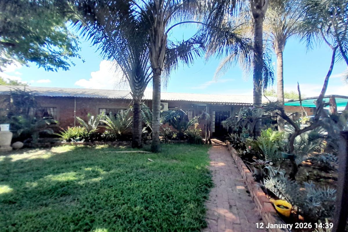 A view of the rear exterior of the farm property, featuring a brick facade, established garden, and a brick-paved pathway leading to the entrance.