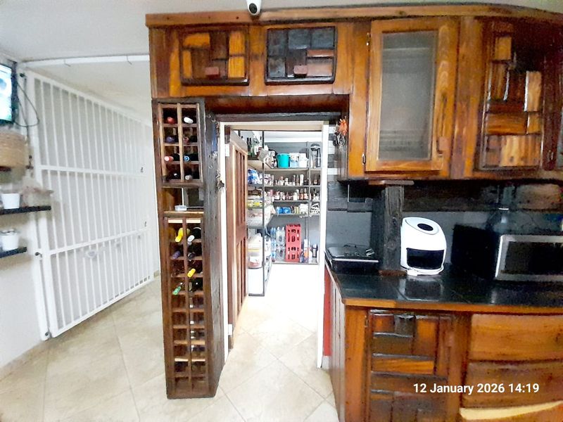A rustic kitchen featuring custom wooden cabinetry, integrated wine storage, and a separate scullery area with tiled flooring.