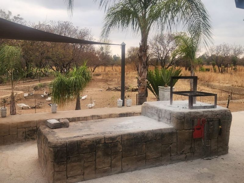 Outdoor entertainment area featuring a built-in stone-clad braai and shade sail, overlooking a rural farm landscape.