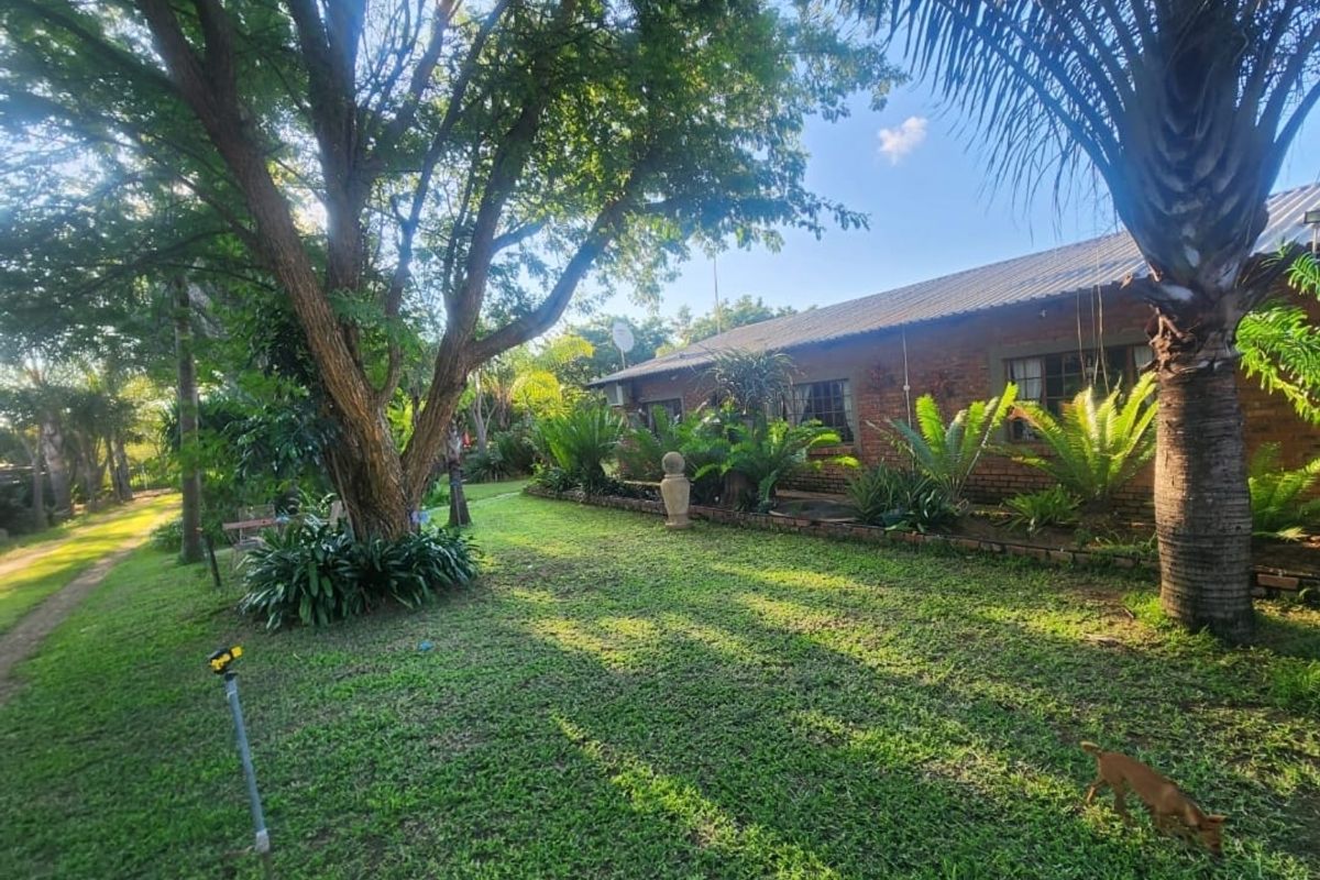 A view of the rear garden and exterior brick facade of the farm property, featuring established trees and landscaped garden beds.