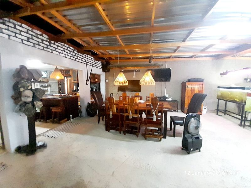 Spacious open-plan living and dining area featuring exposed timber roof beams, rustic brick accents, and direct access to the kitchen space.