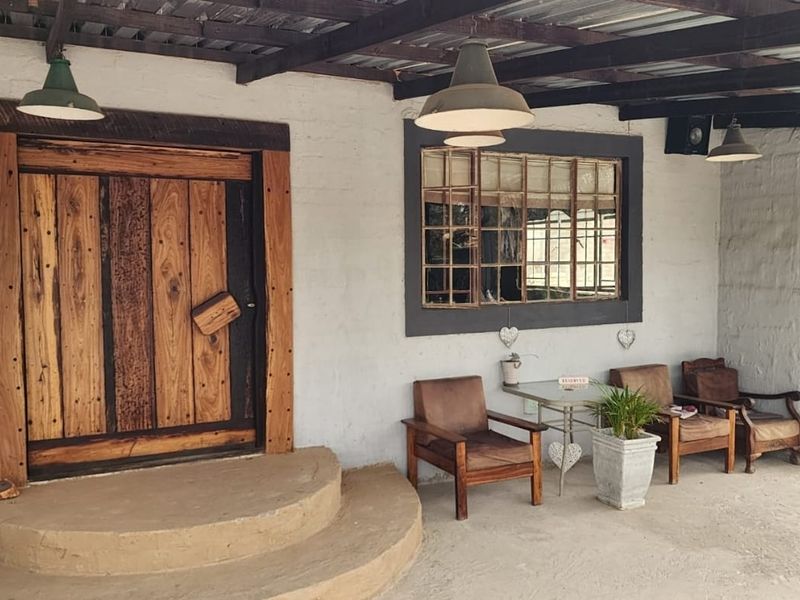 A rustic covered patio area featuring a solid timber entrance door, multi-pane window, and exposed timber beam ceiling structure.