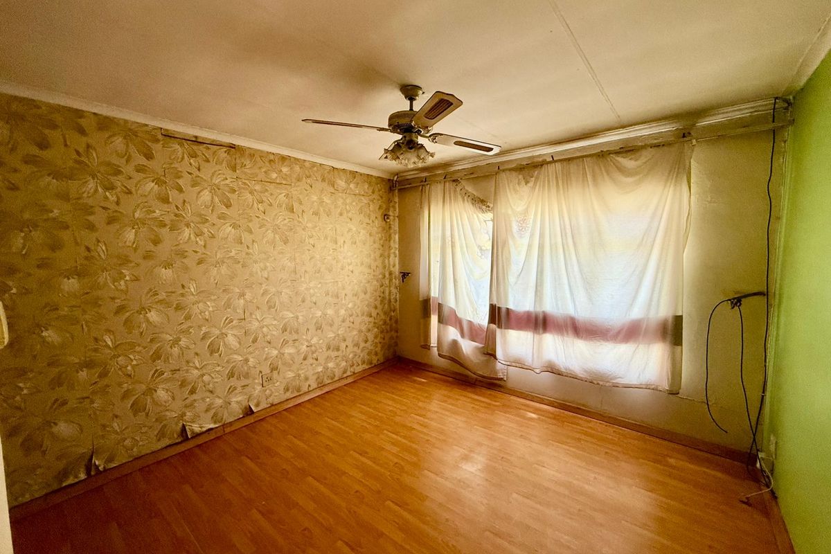 A vacant bedroom featuring wood-look flooring, a ceiling fan, and dated wallpaper, offering a blank canvas for renovation and modernization.