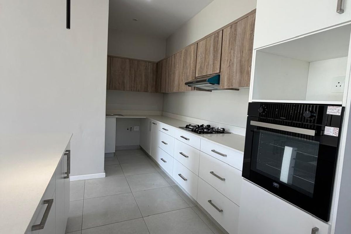 Modern kitchen featuring sleek white cabinetry, wood-grain upper cupboards, stone countertops, a built-in oven, and a gas hob with an extractor fan.