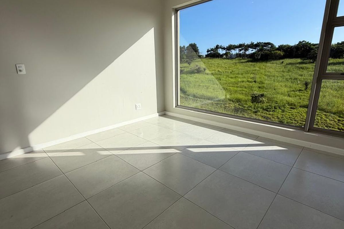 A bright, empty bedroom featuring large windows with scenic green views, neutral tiled flooring, and a modern ceiling fan.
