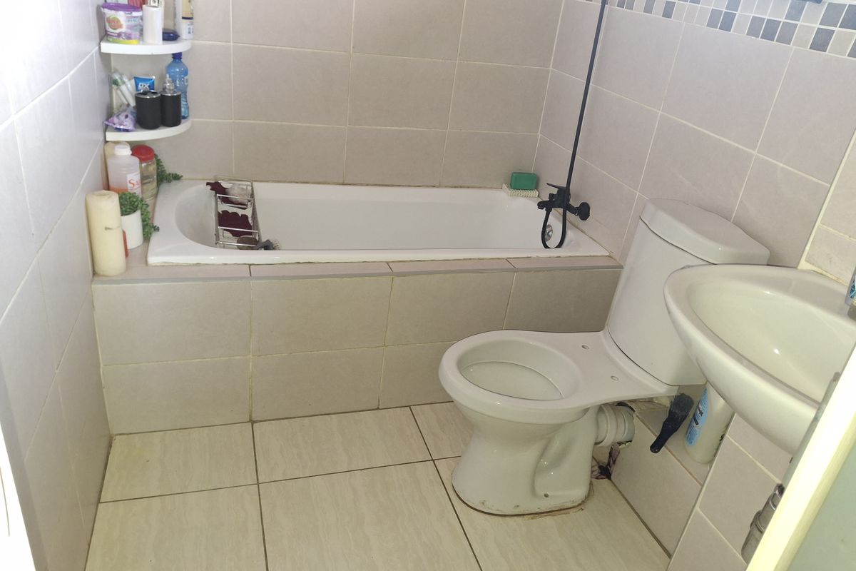 A functional bathroom featuring a built-in bathtub, pedestal washbasin, and toilet, finished with neutral ceramic wall and floor tiles.