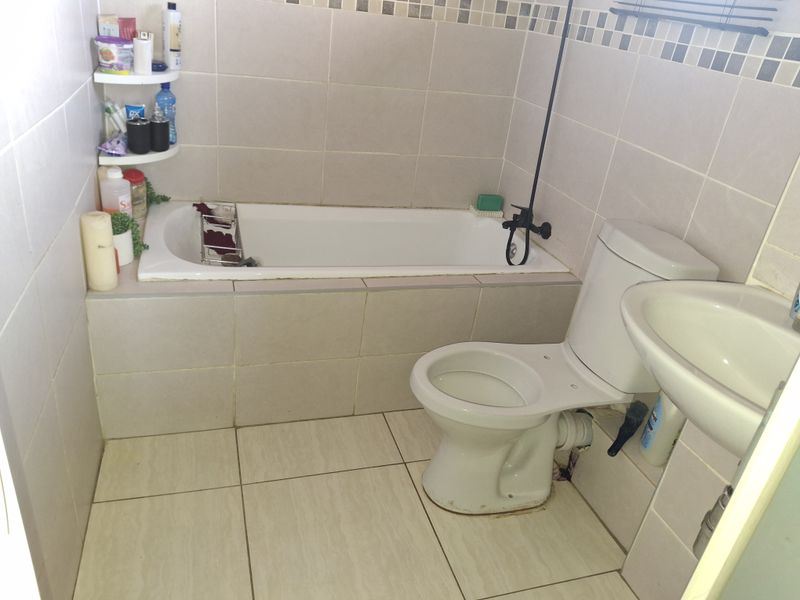 A functional bathroom featuring a built-in bathtub, pedestal washbasin, and toilet, finished with neutral ceramic wall and floor tiles.