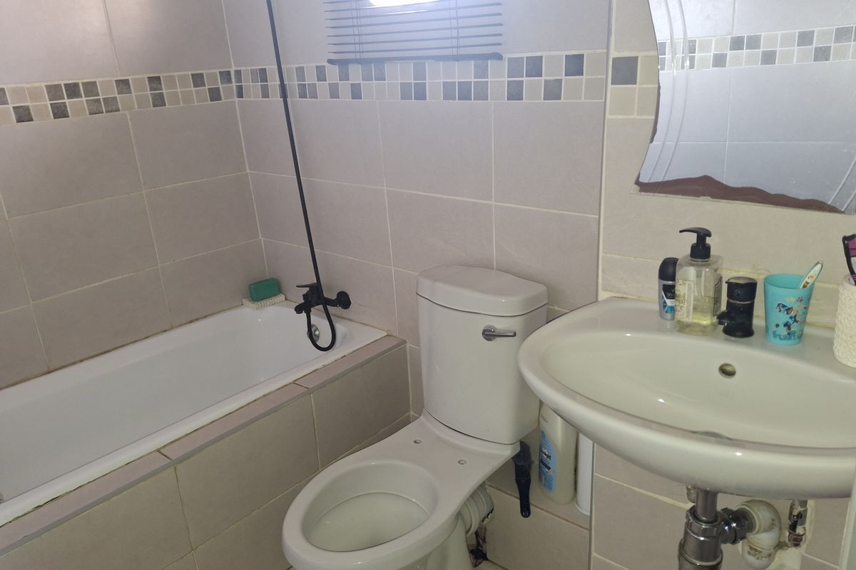 A functional bathroom featuring a built-in bathtub, pedestal washbasin, and ceramic toilet with neutral wall tiling and a decorative mosaic border.