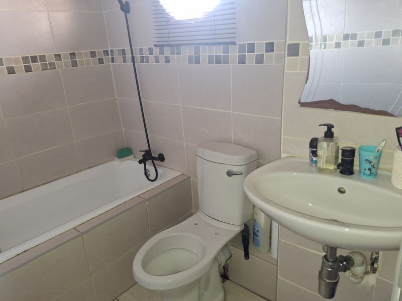 A functional bathroom featuring a built-in bathtub, pedestal washbasin, and ceramic toilet with neutral wall tiling and a decorative mosaic border.