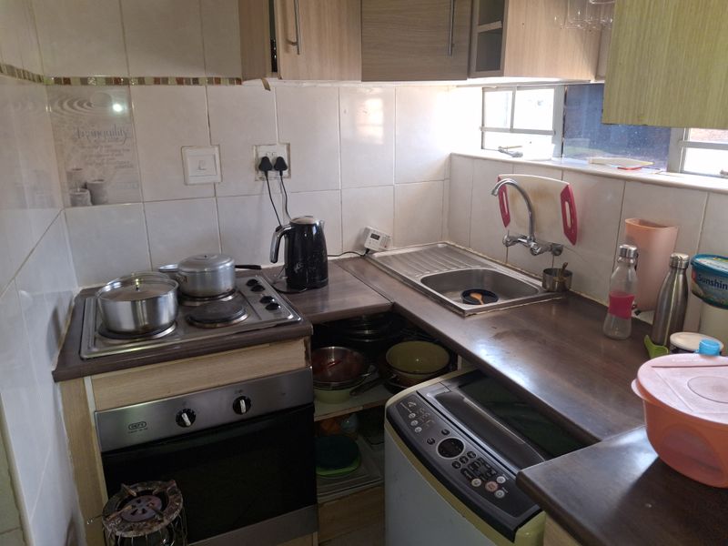 Compact kitchen featuring built-in oven, electric hob, stainless steel sink, and tiled backsplash with overhead cabinetry.