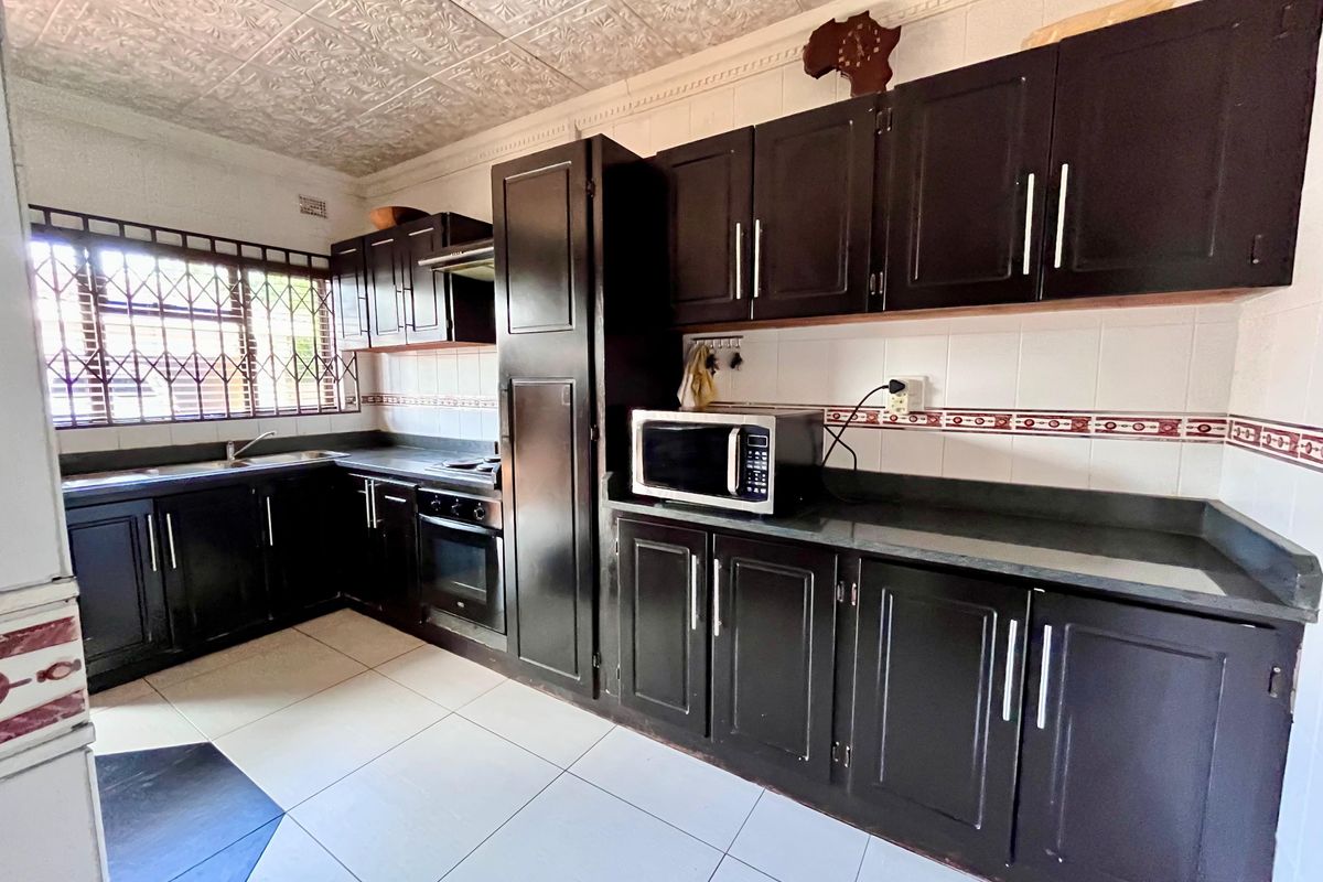 A functional kitchen featuring dark cabinetry, stone-look countertops, tiled backsplash, and a built-in oven with extractor fan.