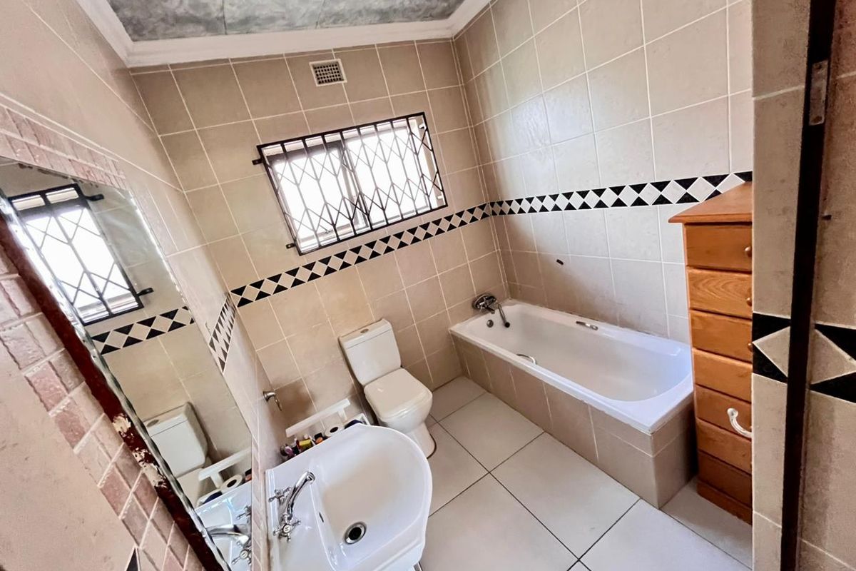 A functional bathroom featuring a bathtub, pedestal basin, and toilet, finished with neutral wall tiles and a decorative border.