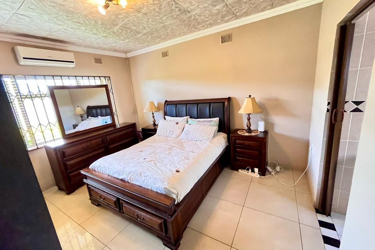 A spacious bedroom featuring tiled flooring, a decorative pressed ceiling, and a wall-mounted air conditioning unit.