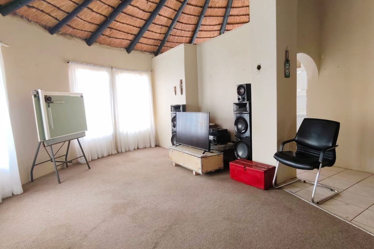 Spacious living area featuring a high vaulted thatched ceiling, neutral walls, and large windows allowing for ample natural light.
