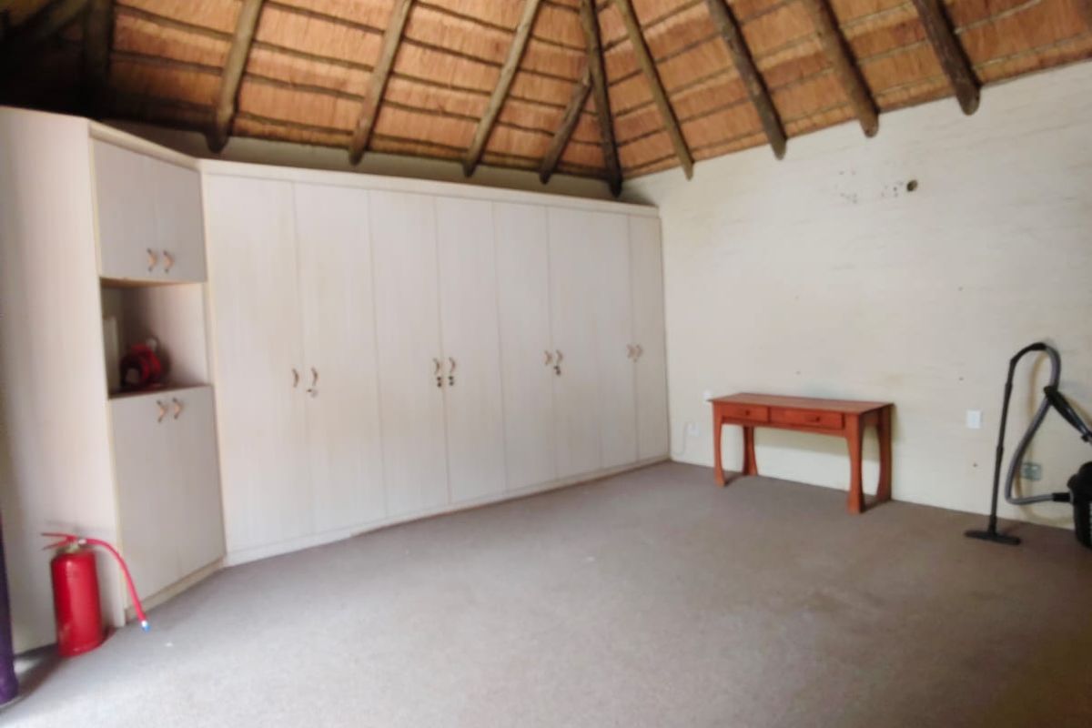 Spacious bedroom featuring a high vaulted thatched ceiling with exposed timber beams, a ceiling fan, and extensive built-in cabinetry.