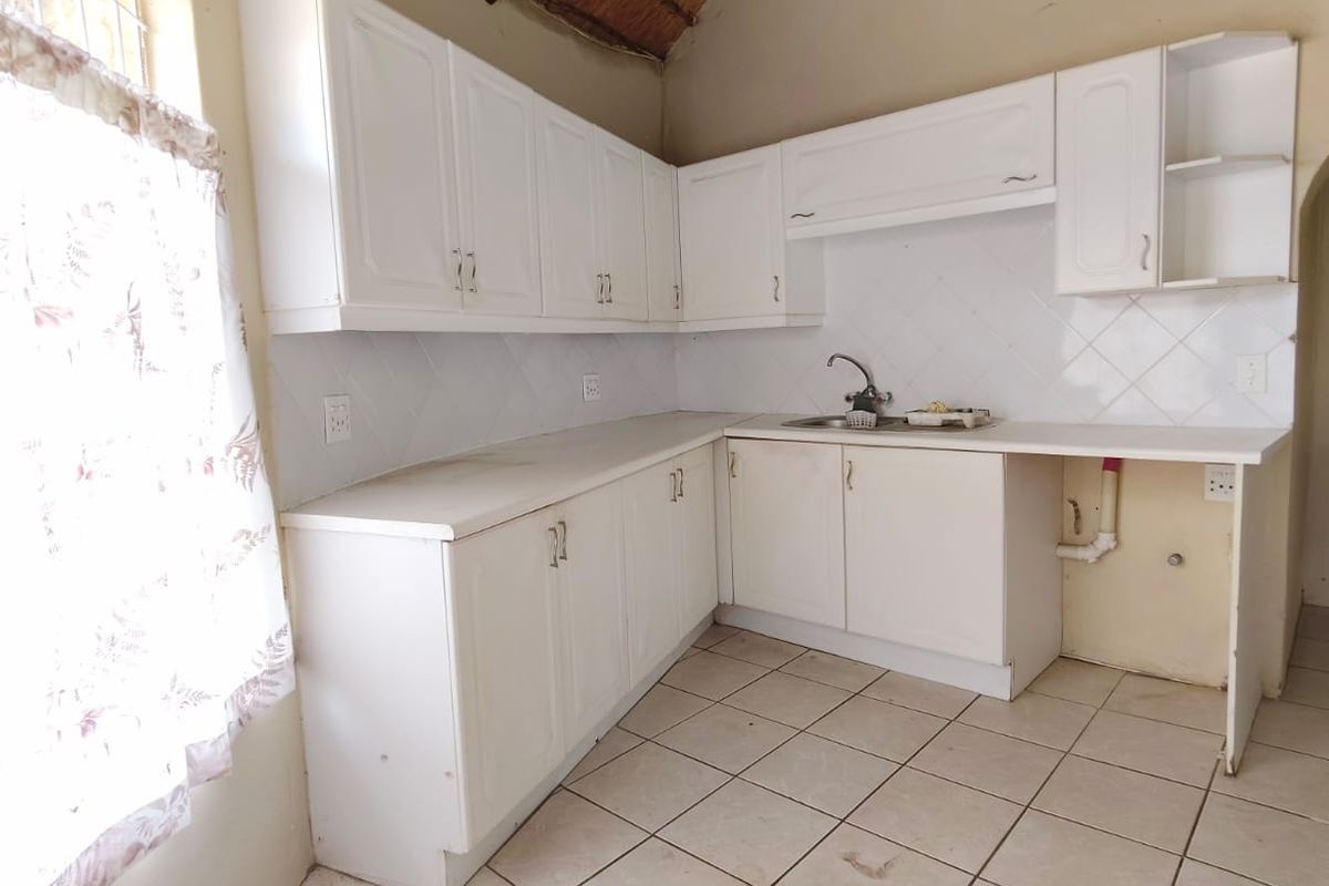 A kitchen featuring white cabinetry, tiled countertops, a stainless steel sink, and a distinctive vaulted thatched ceiling.