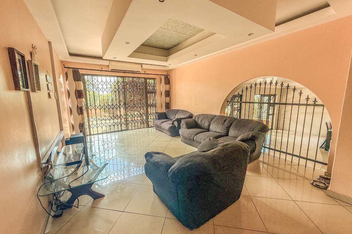 Spacious living room featuring large format floor tiles, a decorative recessed ceiling with downlights, and secure metal security gates on windows and doorways.