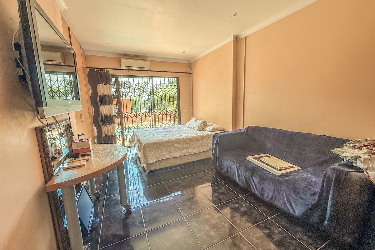 A bedroom featuring dark tiled flooring, a wall-mounted air conditioning unit, and a sliding door with security gate leading to the exterior.