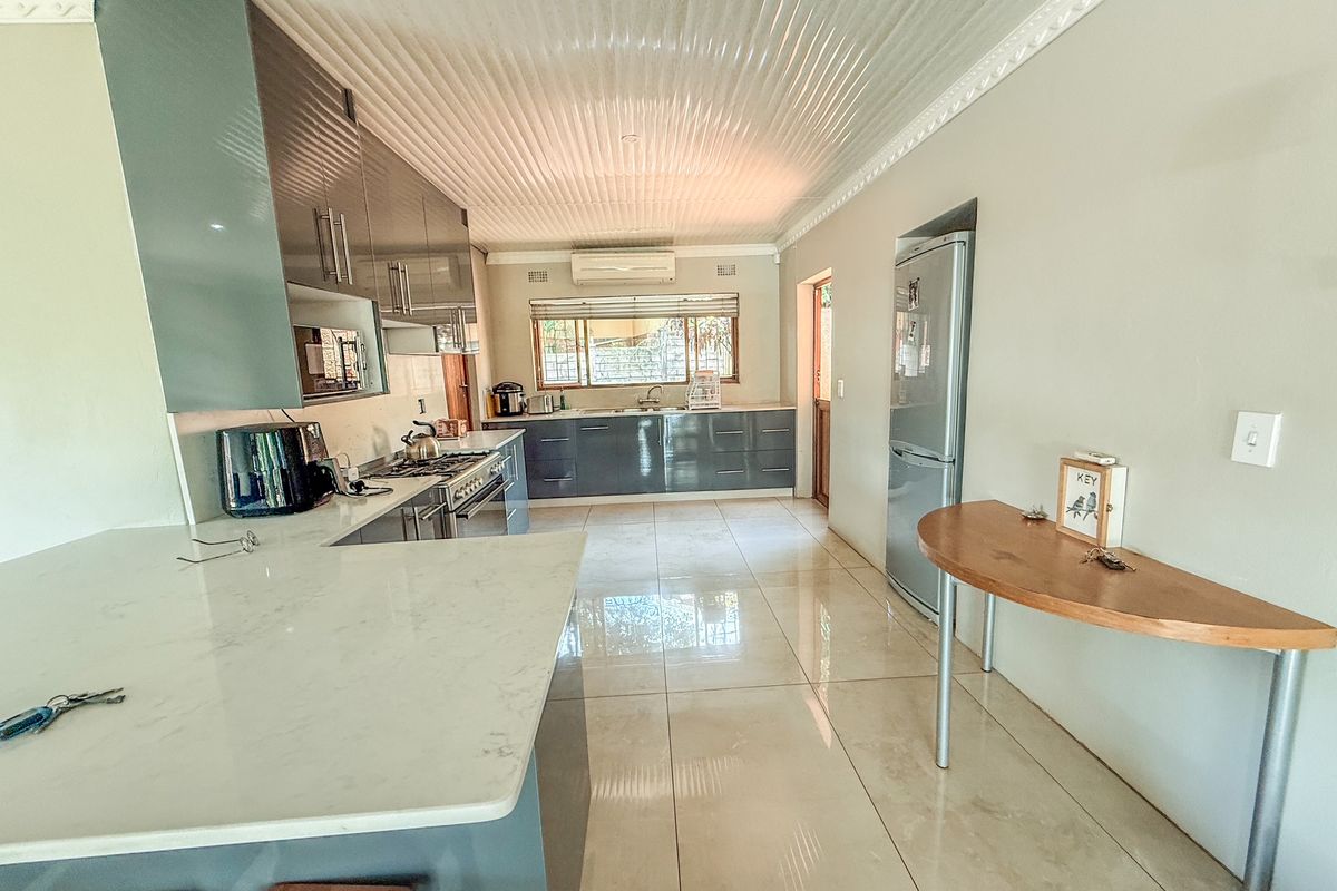 Modern kitchen featuring high-gloss cabinetry, stone countertops, a gas stove, and large format floor tiles, offering a clean and functional culinary space.