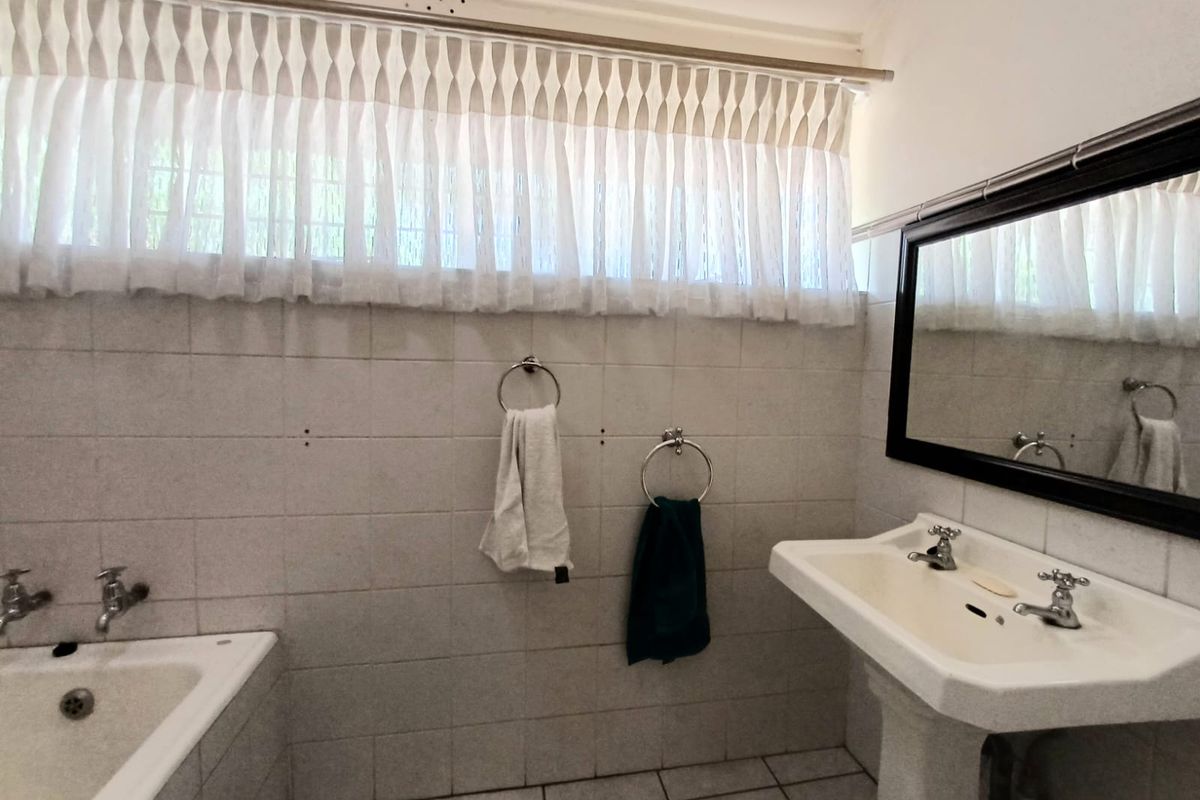 A functional bathroom featuring a pedestal basin, bathtub with chrome taps, and tiled walls, offering a classic layout ready for modernization.