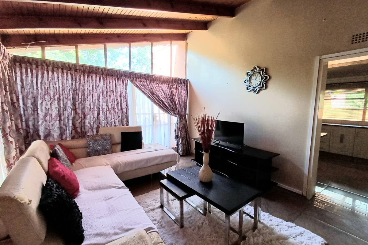 Spacious living room featuring high vaulted timber ceilings, large windows with natural light, and tiled flooring, leading into an adjacent kitchen area.