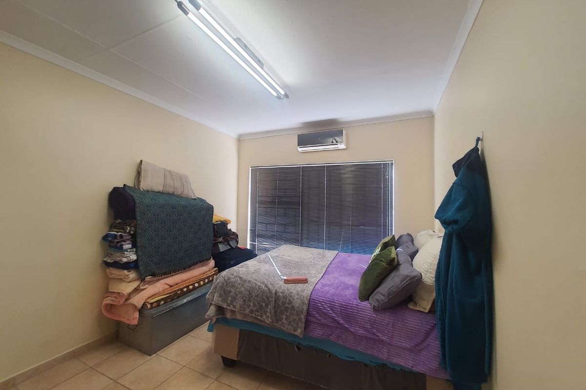A functional bedroom featuring tiled flooring, a wall-mounted air conditioning unit, and horizontal window blinds.