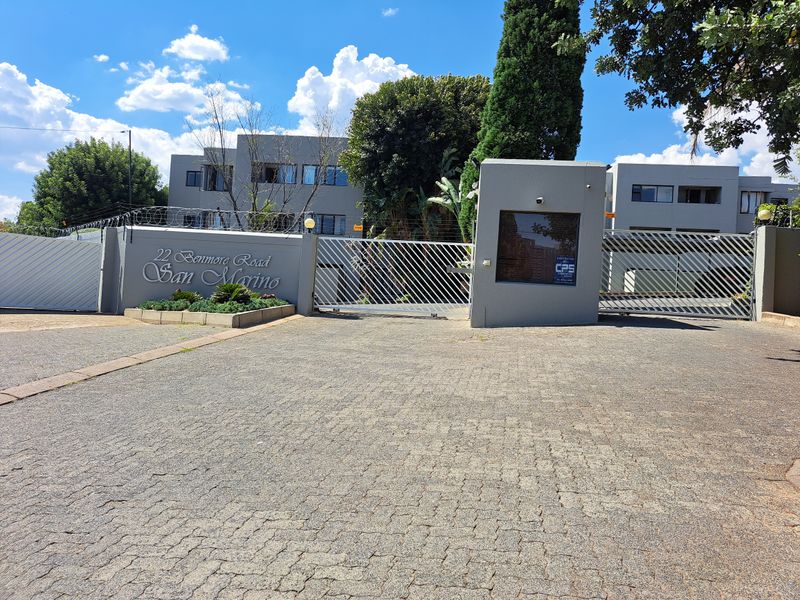 Front entrance view of the San Marino apartment complex, featuring a paved driveway, secure gated access, and a dedicated guard house.