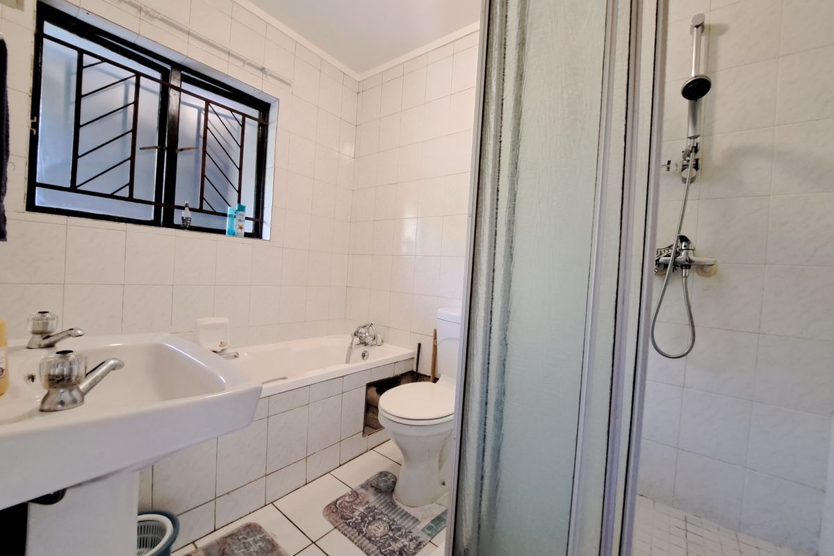 A functional bathroom featuring a pedestal basin, bathtub, toilet, and separate shower enclosure with tiled finishes and security bars on the window.