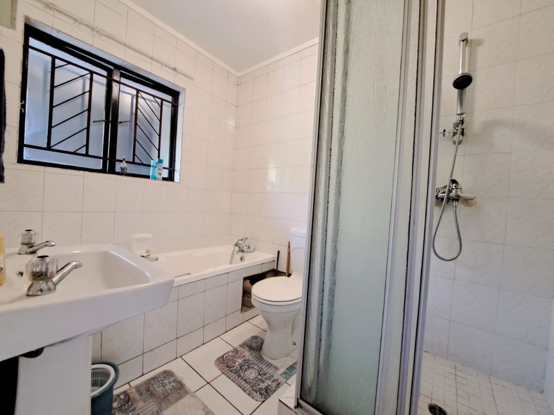 A functional bathroom featuring a pedestal basin, bathtub, toilet, and separate shower enclosure with tiled finishes and security bars on the window.