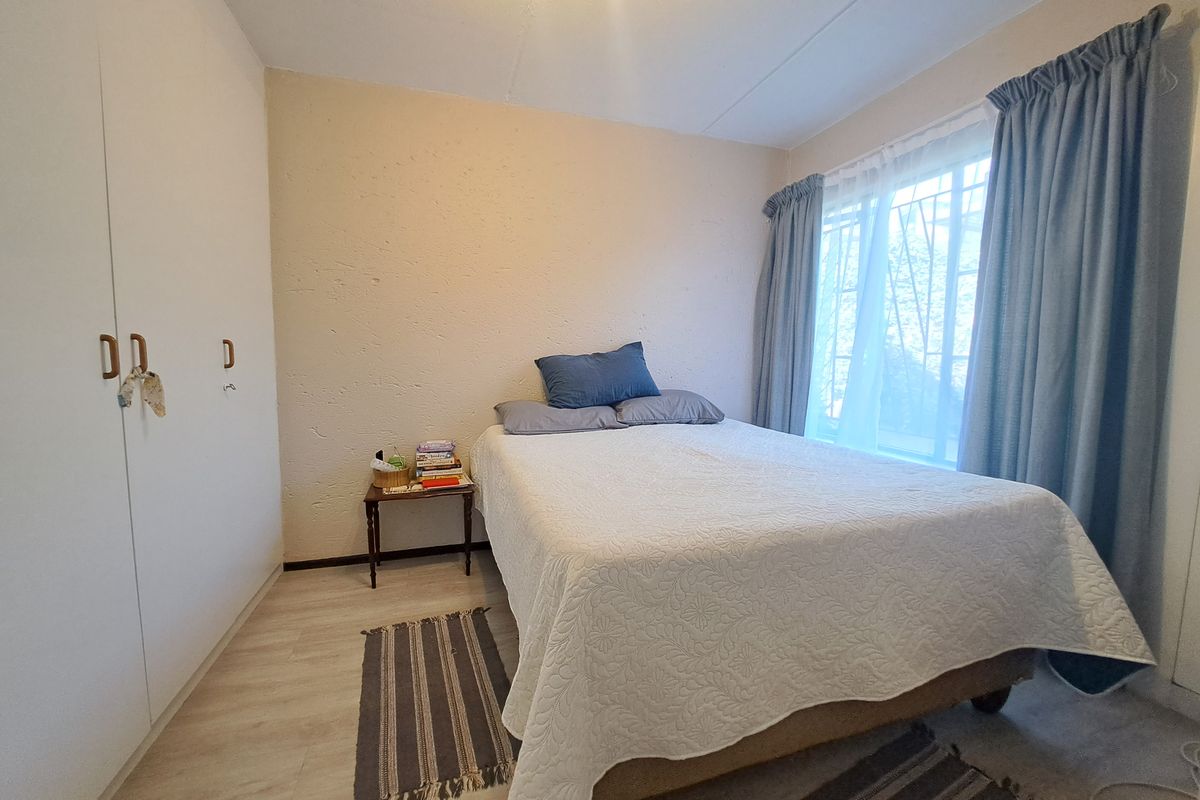 A functional bedroom featuring light laminate flooring, built-in cupboards for storage, and a window fitted with security bars.