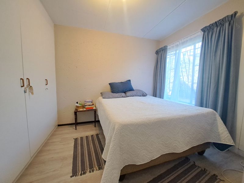 A functional bedroom featuring light laminate flooring, built-in cupboards for storage, and a window fitted with security bars.